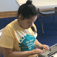 Student sits at a table and completes her spelling contest at the NJ Regional Braille Challenge