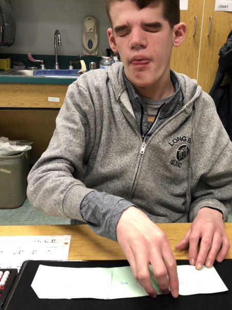 student sits at a desk and reads braille key word flashcards